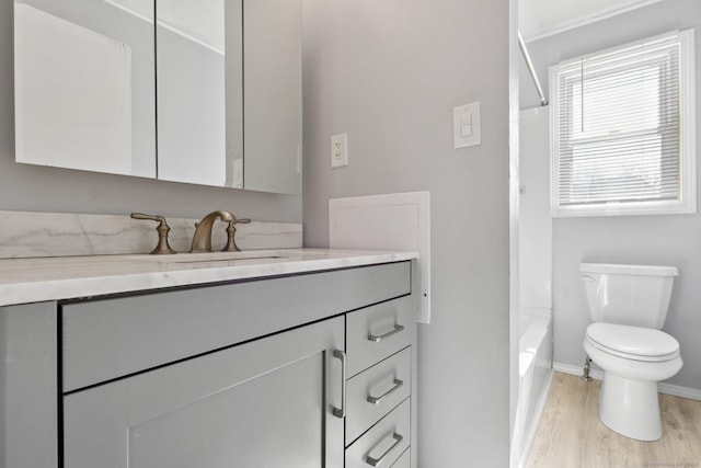 bathroom featuring baseboards, toilet, vanity, wood finished floors, and washtub / shower combination