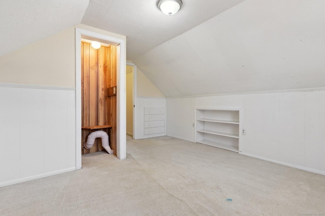 additional living space with a textured ceiling, built in shelves, carpet, and vaulted ceiling