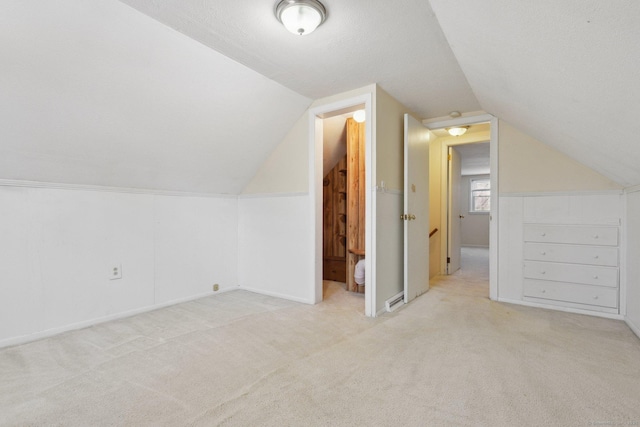 additional living space featuring visible vents, a textured ceiling, lofted ceiling, and carpet