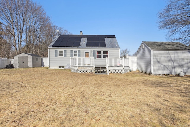 rear view of property featuring an outbuilding, a wooden deck, a storage unit, a lawn, and roof mounted solar panels