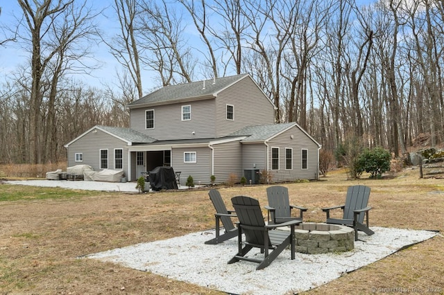 back of property featuring a patio, central AC unit, a yard, a shingled roof, and a fire pit