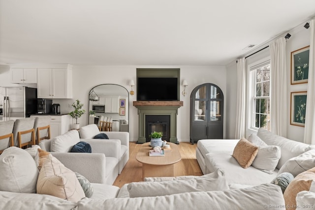 living area with a glass covered fireplace, wood finished floors, visible vents, and ornamental molding