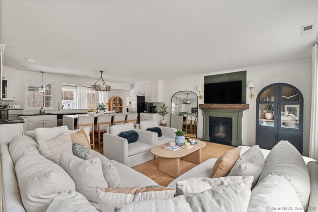 living area with light wood finished floors, visible vents, crown molding, a chandelier, and a glass covered fireplace