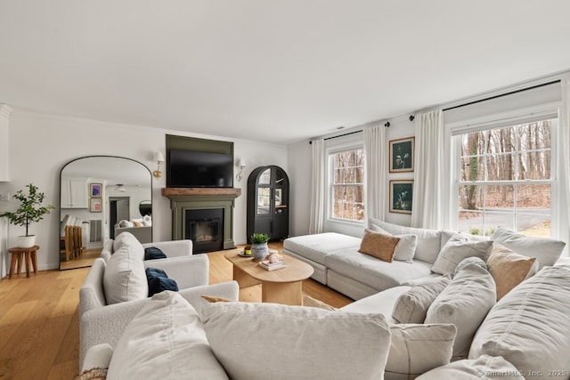 living room featuring visible vents, a glass covered fireplace, light wood-style floors, crown molding, and baseboards