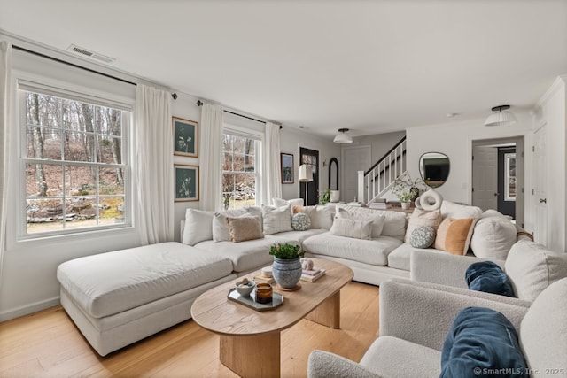 living room with stairway, light wood-style flooring, visible vents, and baseboards