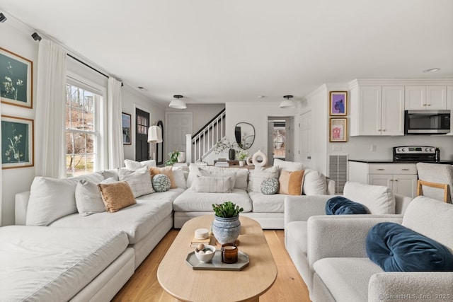 living area with stairs, crown molding, visible vents, and light wood-type flooring