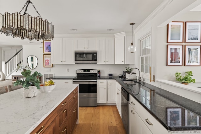 kitchen featuring light wood-type flooring, a sink, decorative light fixtures, white cabinetry, and appliances with stainless steel finishes