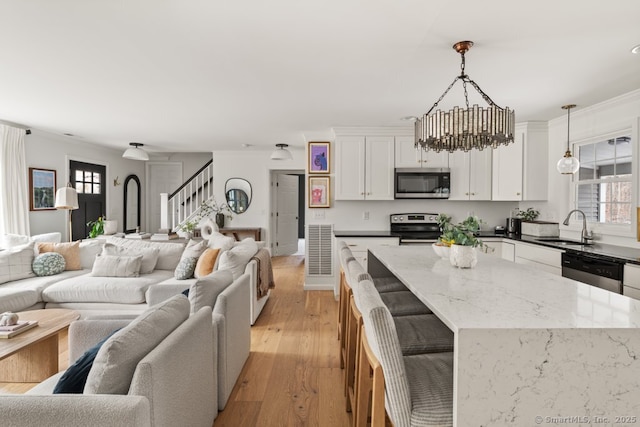 kitchen featuring open floor plan, light wood-style flooring, appliances with stainless steel finishes, white cabinets, and a sink