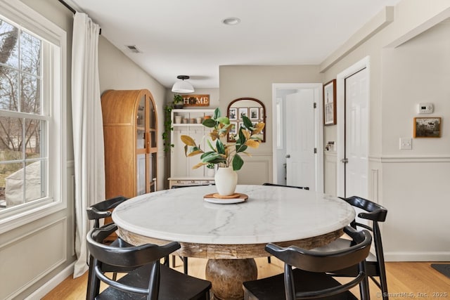 dining room with a decorative wall, light wood-style floors, and visible vents