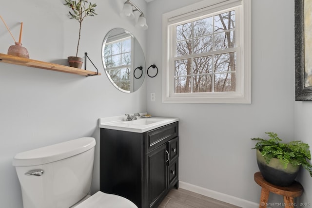 half bath with vanity, toilet, wood finished floors, and baseboards