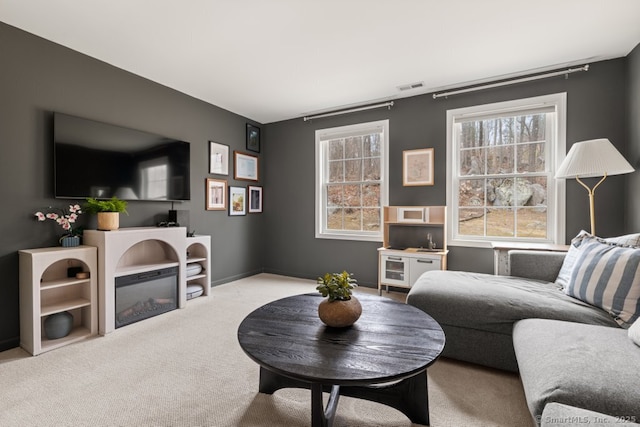 living room with a glass covered fireplace, carpet, visible vents, and baseboards