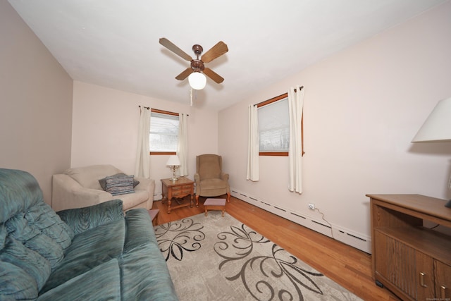 living area with light wood-style floors, baseboard heating, and ceiling fan