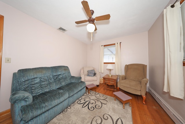 living room featuring visible vents, baseboards, baseboard heating, wood finished floors, and a ceiling fan