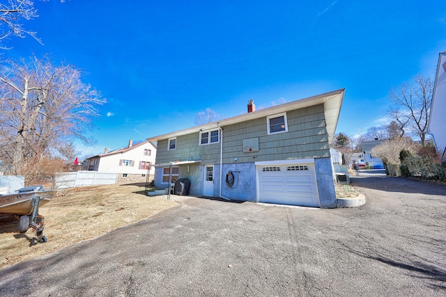 rear view of property with aphalt driveway, a chimney, an attached garage, and fence