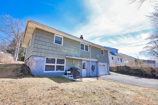 back of house featuring driveway, a chimney, and a garage