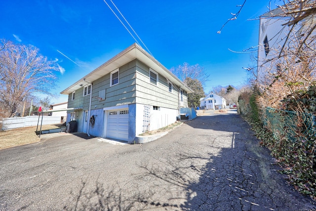 view of side of property featuring driveway, a garage, and fence