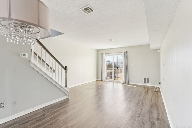 unfurnished living room featuring visible vents, a textured ceiling, wood finished floors, and stairway