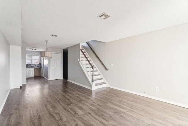 unfurnished living room featuring stairway, dark wood-style floors, visible vents, baseboards, and a textured ceiling