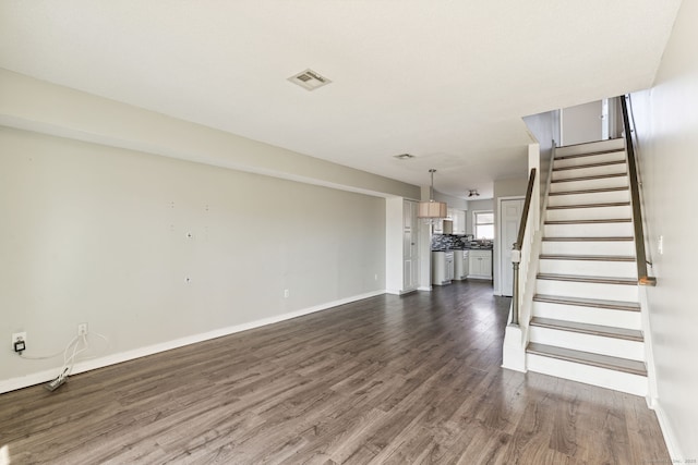 unfurnished living room with dark wood finished floors, visible vents, stairway, and baseboards