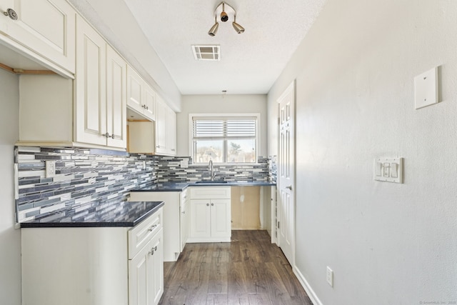 kitchen featuring visible vents, a sink, tasteful backsplash, dark countertops, and dark wood-style flooring