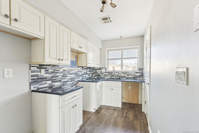 kitchen with visible vents, dark wood-type flooring, a sink, dark countertops, and decorative backsplash