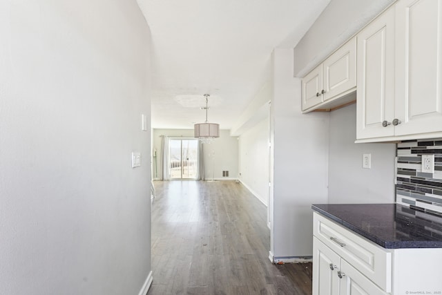 kitchen with tasteful backsplash, dark countertops, dark wood finished floors, white cabinetry, and baseboards