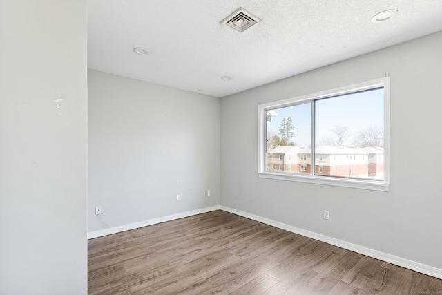 unfurnished room featuring visible vents, a textured ceiling, baseboards, and wood finished floors