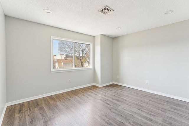 empty room with a textured ceiling, wood finished floors, visible vents, and baseboards