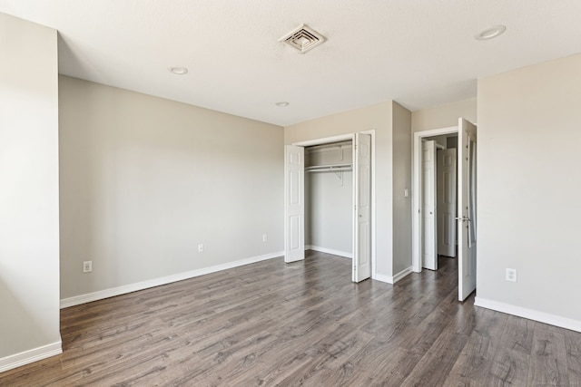 unfurnished bedroom with dark wood-style floors, visible vents, a closet, and baseboards