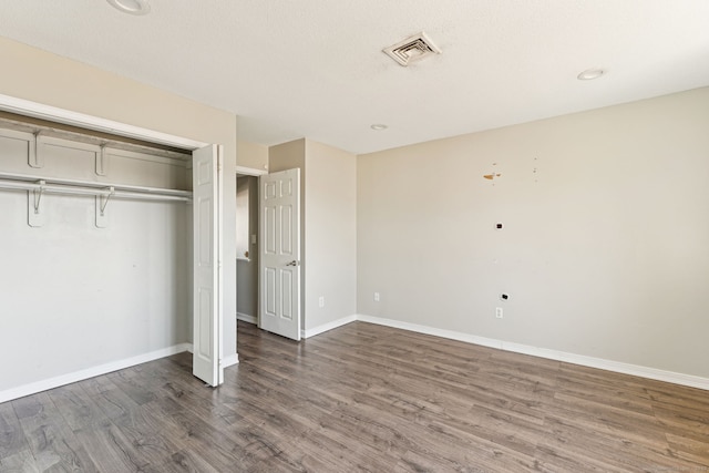 unfurnished bedroom with visible vents, wood finished floors, baseboards, and a closet