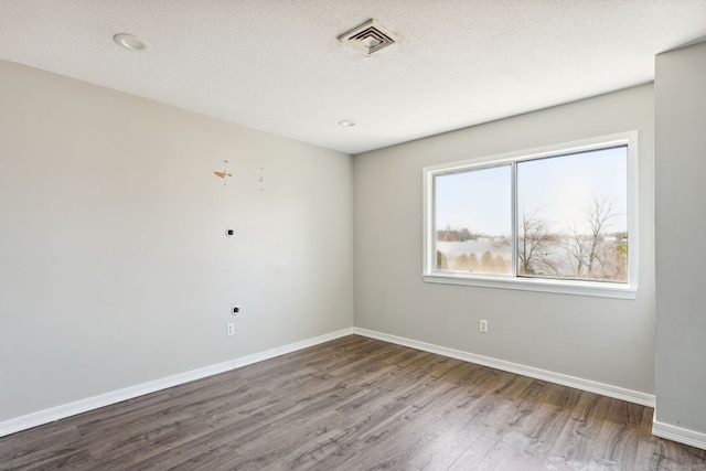 unfurnished room with wood finished floors, baseboards, visible vents, and a textured ceiling