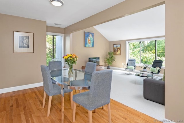dining room with wood finished floors, vaulted ceiling, baseboards, and visible vents