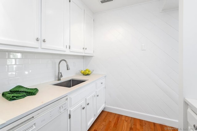 kitchen featuring a sink, tasteful backsplash, white cabinets, white dishwasher, and light countertops