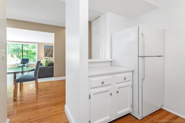 kitchen with baseboards, light countertops, light wood-style flooring, freestanding refrigerator, and white cabinetry