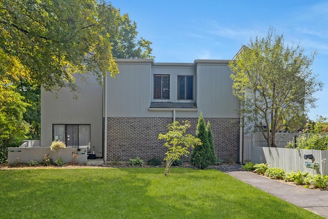 rear view of property featuring fence, brick siding, and a yard
