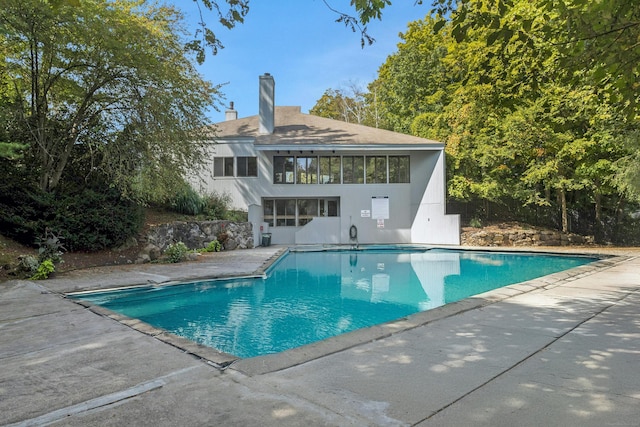 rear view of house with an outdoor pool, a chimney, a patio area, and stucco siding