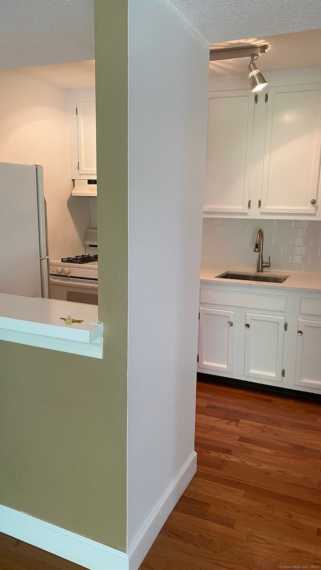 kitchen with a sink, freestanding refrigerator, white cabinets, under cabinet range hood, and gas range gas stove
