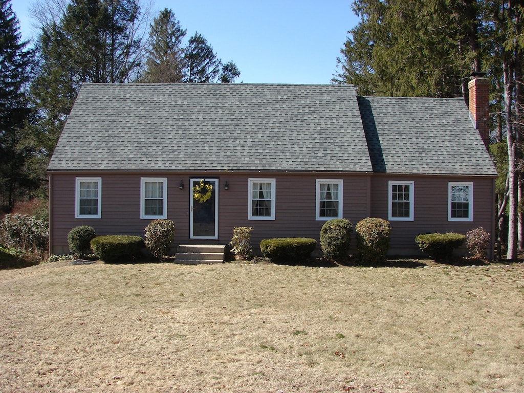 view of front of house with entry steps, a front yard, roof with shingles, and a chimney