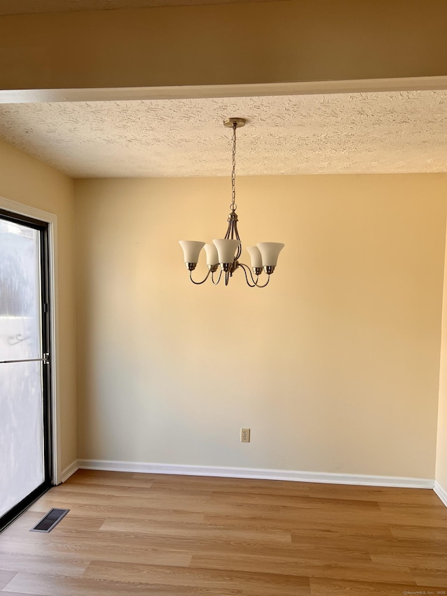 unfurnished dining area featuring visible vents, baseboards, light wood-style floors, and a chandelier