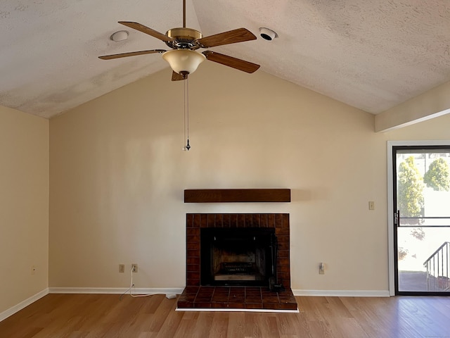 unfurnished living room featuring lofted ceiling, a textured ceiling, a fireplace with raised hearth, and wood finished floors