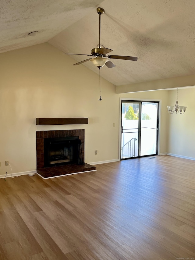 unfurnished living room with lofted ceiling, a textured ceiling, a brick fireplace, and wood finished floors