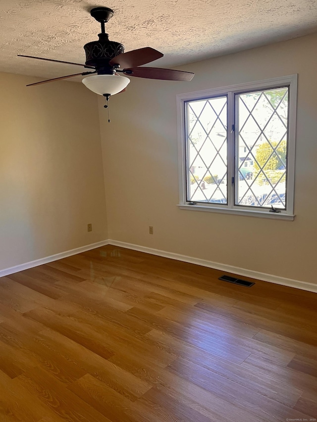 empty room featuring visible vents, baseboards, a textured ceiling, and wood finished floors