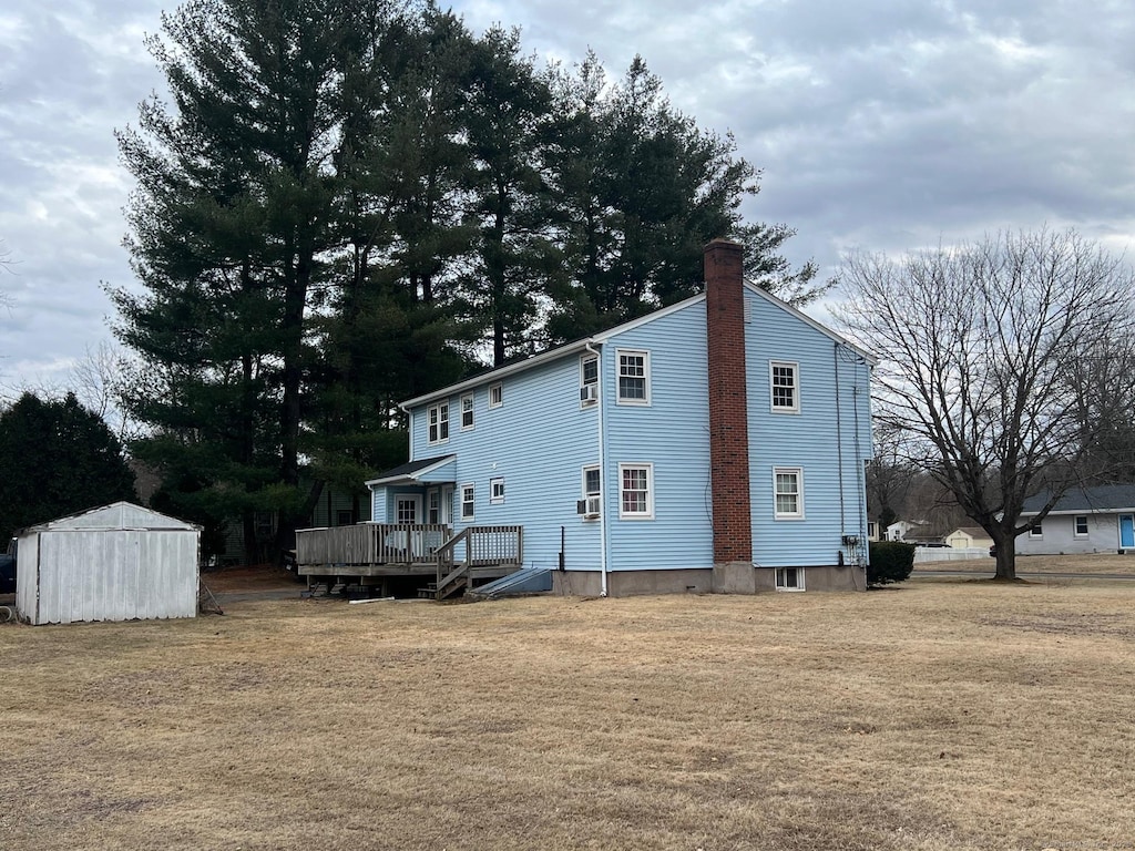 rear view of property with a storage unit, an outbuilding, a yard, and a chimney