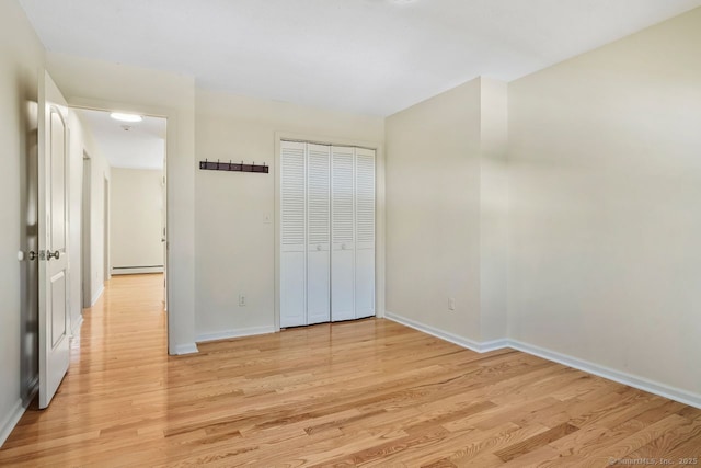 unfurnished bedroom featuring a baseboard heating unit, baseboards, light wood-style floors, and a closet