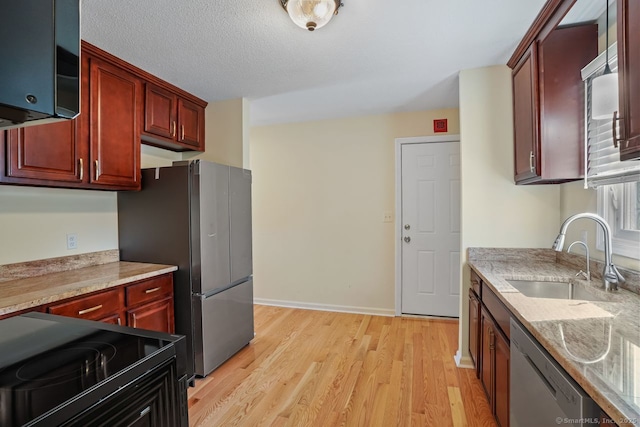 kitchen with light wood finished floors, stainless steel appliances, a sink, dark brown cabinets, and a textured ceiling