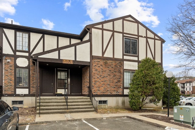 english style home featuring uncovered parking, brick siding, and stucco siding