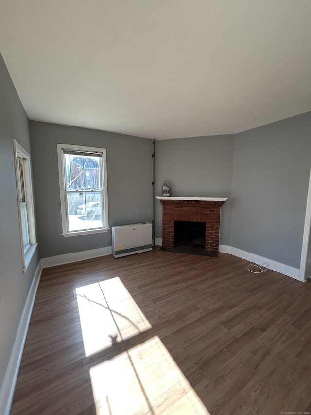 unfurnished living room with a brick fireplace, dark wood-type flooring, and baseboards