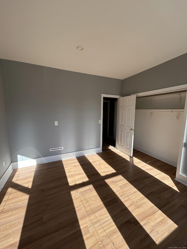 unfurnished bedroom with a closet, baseboards, and dark wood-style flooring