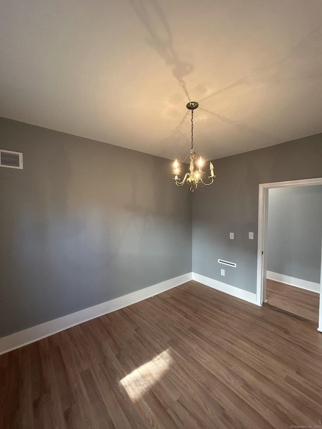 empty room featuring a notable chandelier, baseboards, dark wood-type flooring, and visible vents