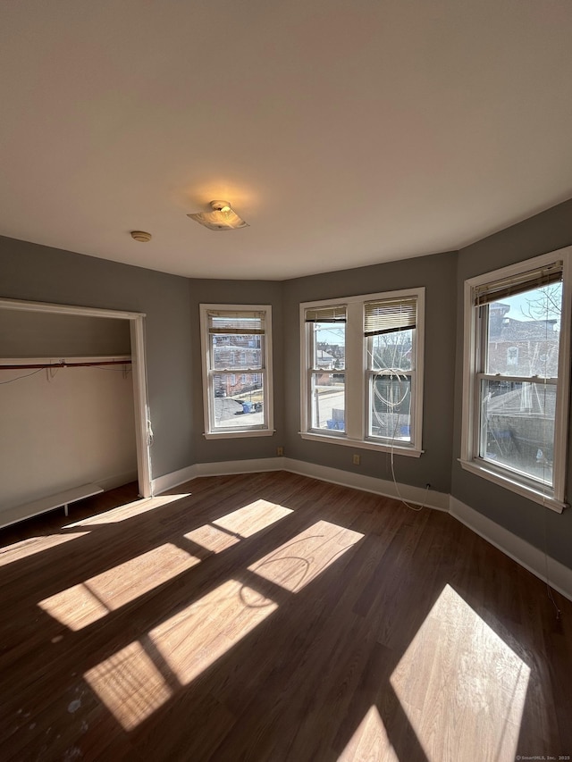 unfurnished bedroom with a closet, dark wood-type flooring, and baseboards